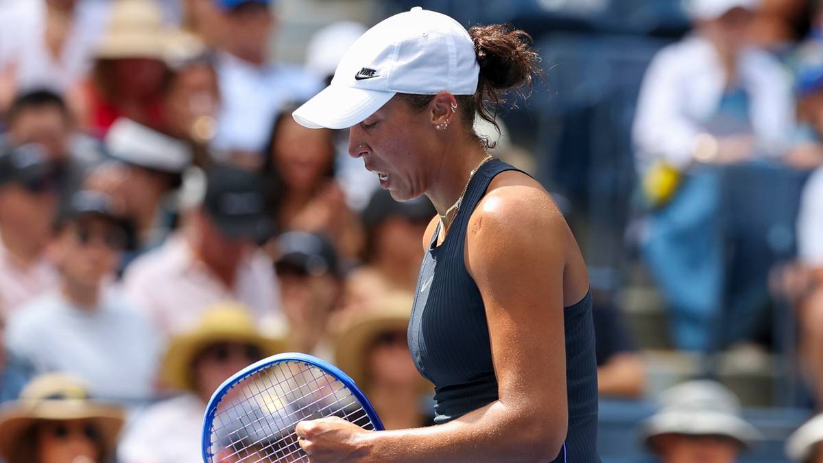 Tenisistka w białej czapce i czarnej sukience trzyma rakietę w ręku, patrząc w dół z determinacją.