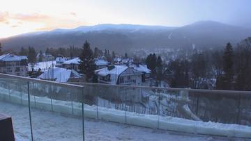 Krajobraz zimowy z ośnieżonymi domami i g&oacute;rami w tle.