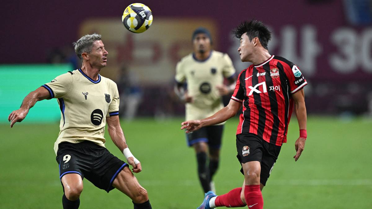 Piłkarz Robert Lewandowski w żółtej koszulce, wpatrzony w piłkę nad głową, podczas meczu. Naprzeciwko niego stoi przeciwnik w czarno-czerwonej koszulce.