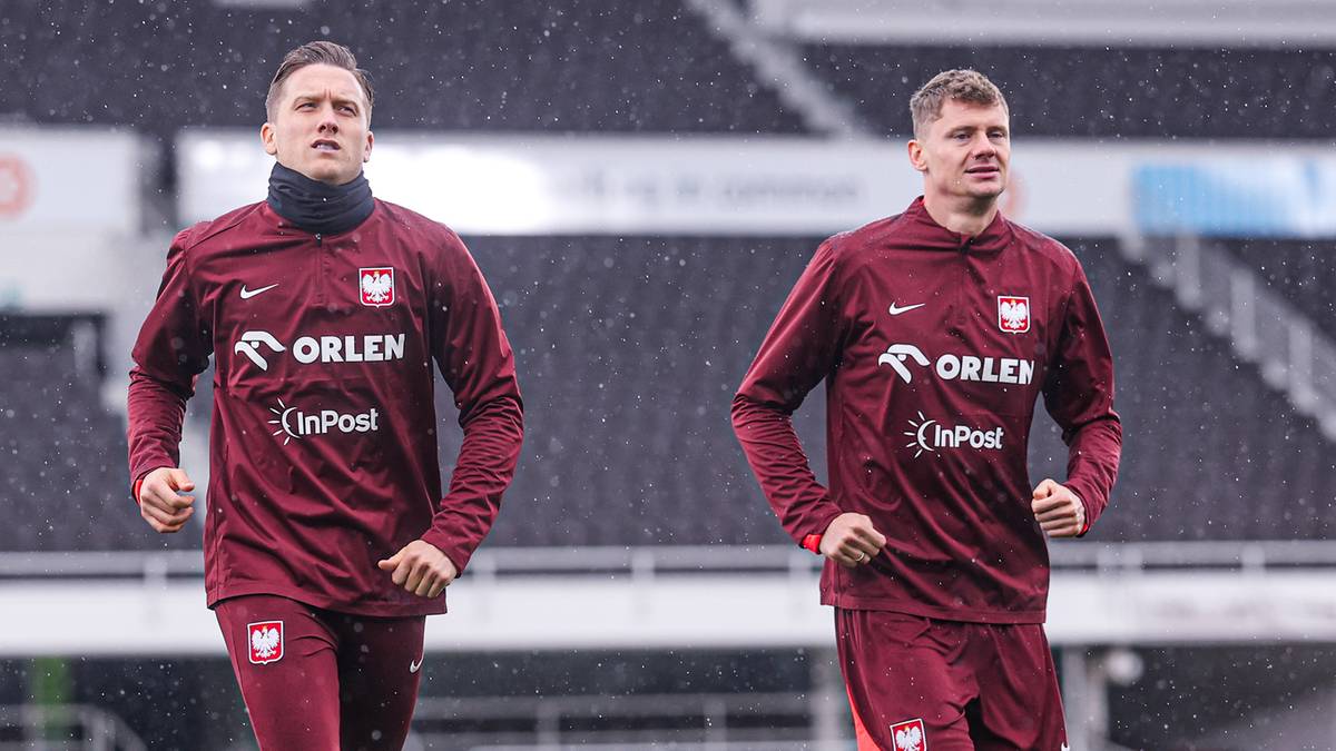 Dw&oacute;ch piłkarzy reprezentacji Polski w bordowych strojach treningowych biegnie po boisku stadionu.