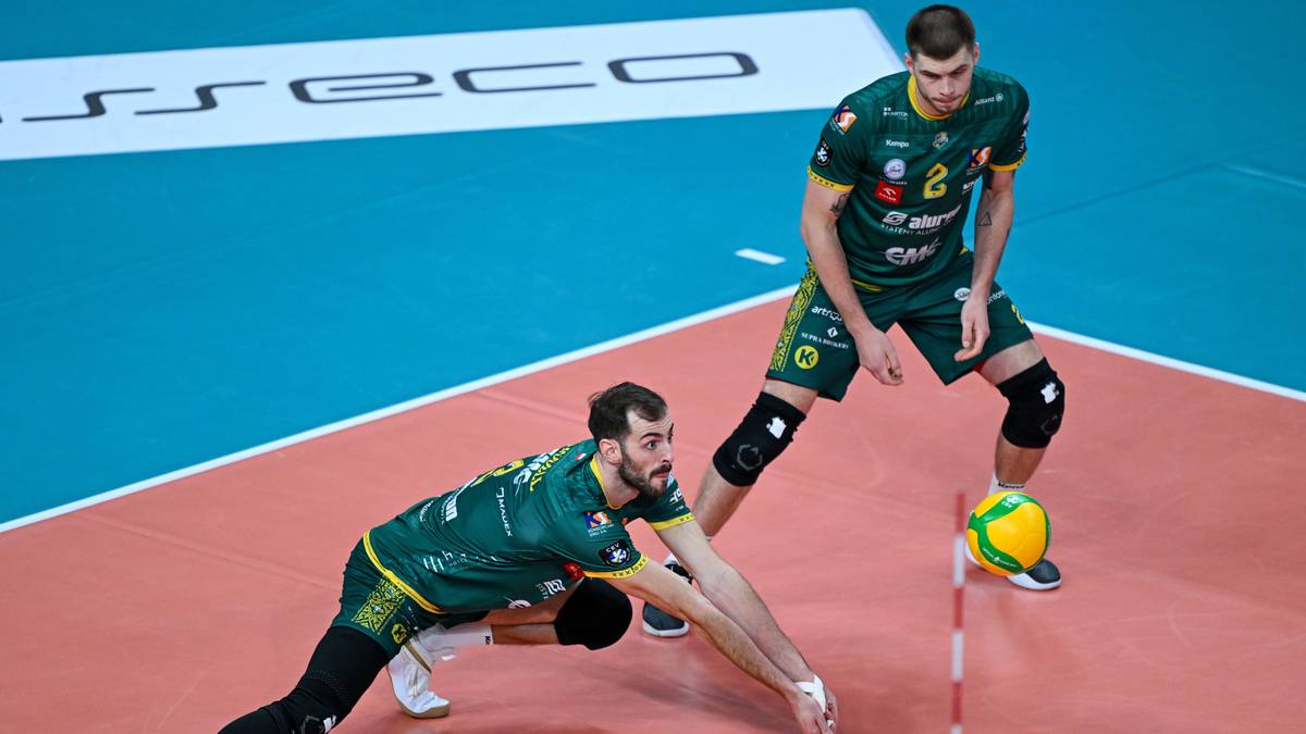 Dw&oacute;ch siatkarzy w zielonych strojach rywalizuje o piłkę na boisku.