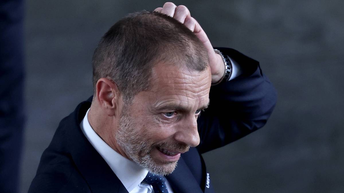 Prezydent UEFA Aleksander Čeferin w garniturze, wykonujący gest ręką przy włosach.
