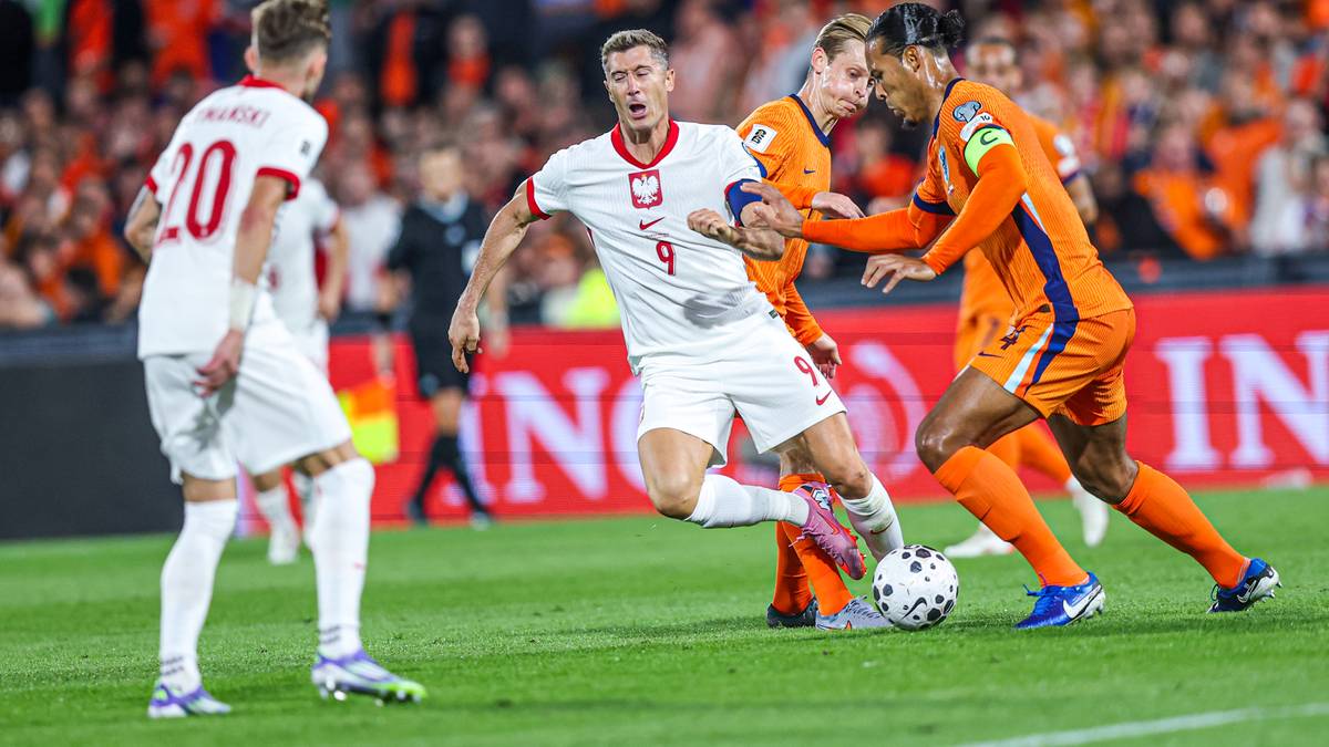 Piłkarze reprezentacji Polski w białych strojach walczą o piłkę z zawodnikami Holandii w pomarańczowych strojach.