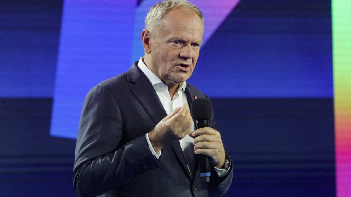 Mężczyzna w garniturze przemawia z mikrofonem na tle kolorowej sceny