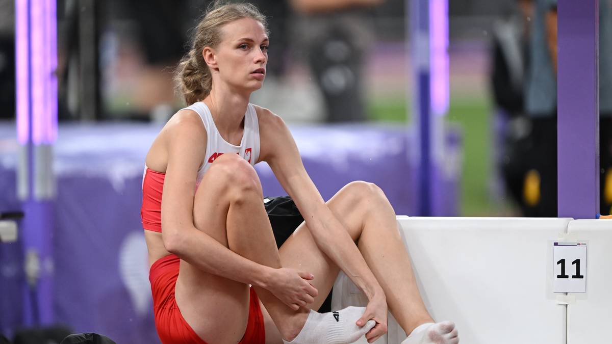Sportsmenka siedzi na ławce, ubrana w czerwono-biały str&oacute;j sportowy.