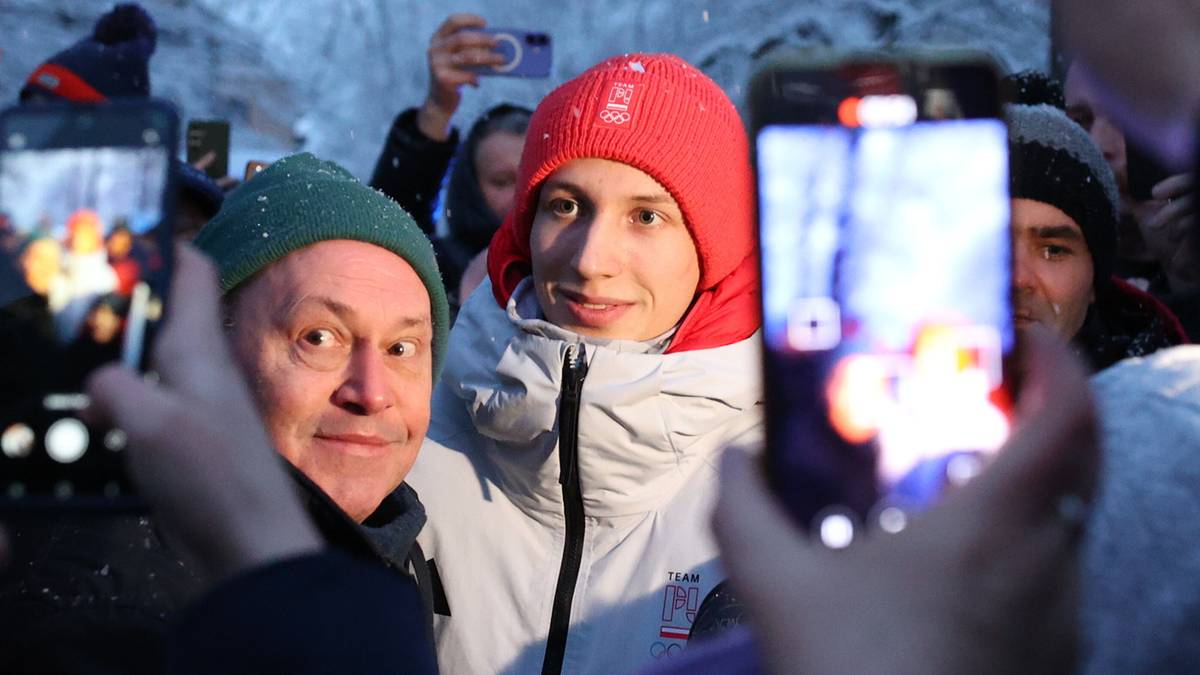 Ludzie w zimowym otoczeniu z drzewami pokrytymi szronem, trzymający smartfony i robiący zdjęcia.