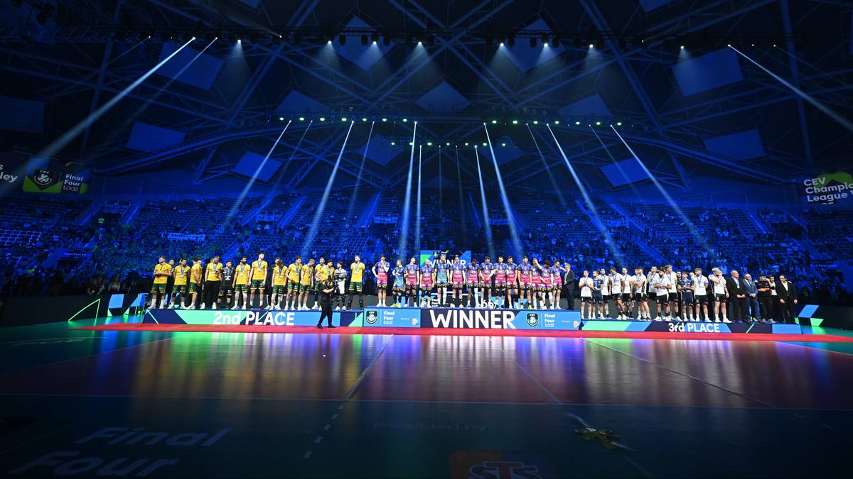 Drużyna siatkarska świętuje zwycięstwo na scenie z napisem "WINNER", oświetlonej niebieskimi światłami.