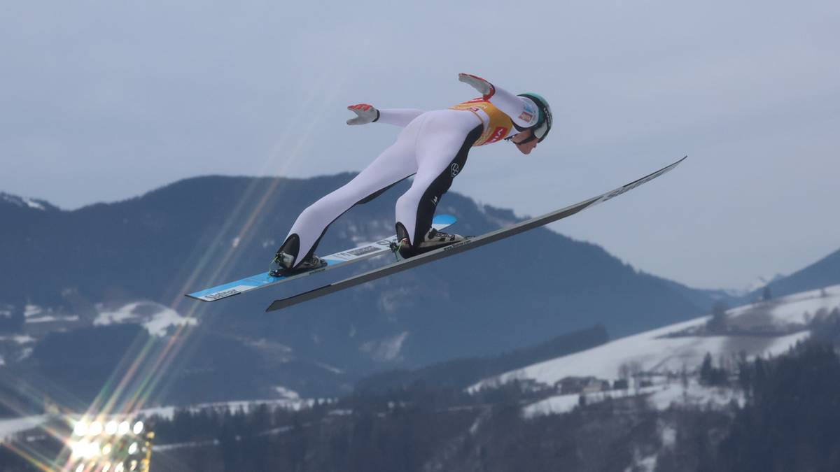 Skoczek narciarski w locie na tle g&oacute;rskiego krajobrazu nocą.