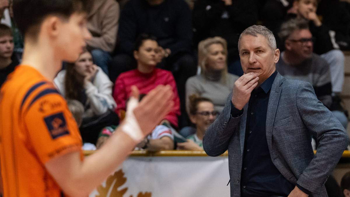 Siatkarz w pomarańczowej koszulce rozmawia z trenerem w garniturze.