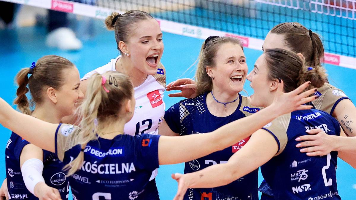 Grupa zawodniczek siatk&oacute;wki w ciemnych strojach świętuje na boisku, przytulając się i śmiejąc.