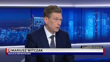 Mężczyzna w garniturze, Mariusz Witczak, przemawia podczas programu telewizyjnego. W tle widoczne jest miejskie nocne niebo.