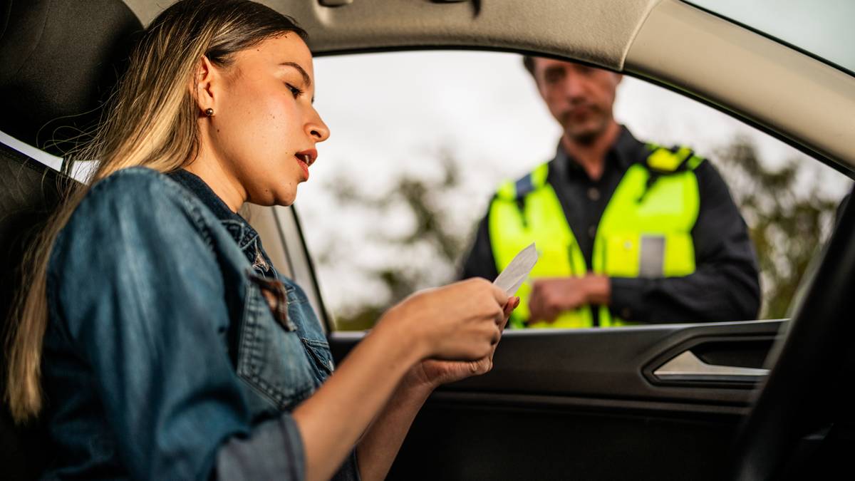 Kobieta w samochodzie pokazuje dokument policjantowi w kamizelce odblaskowej.
