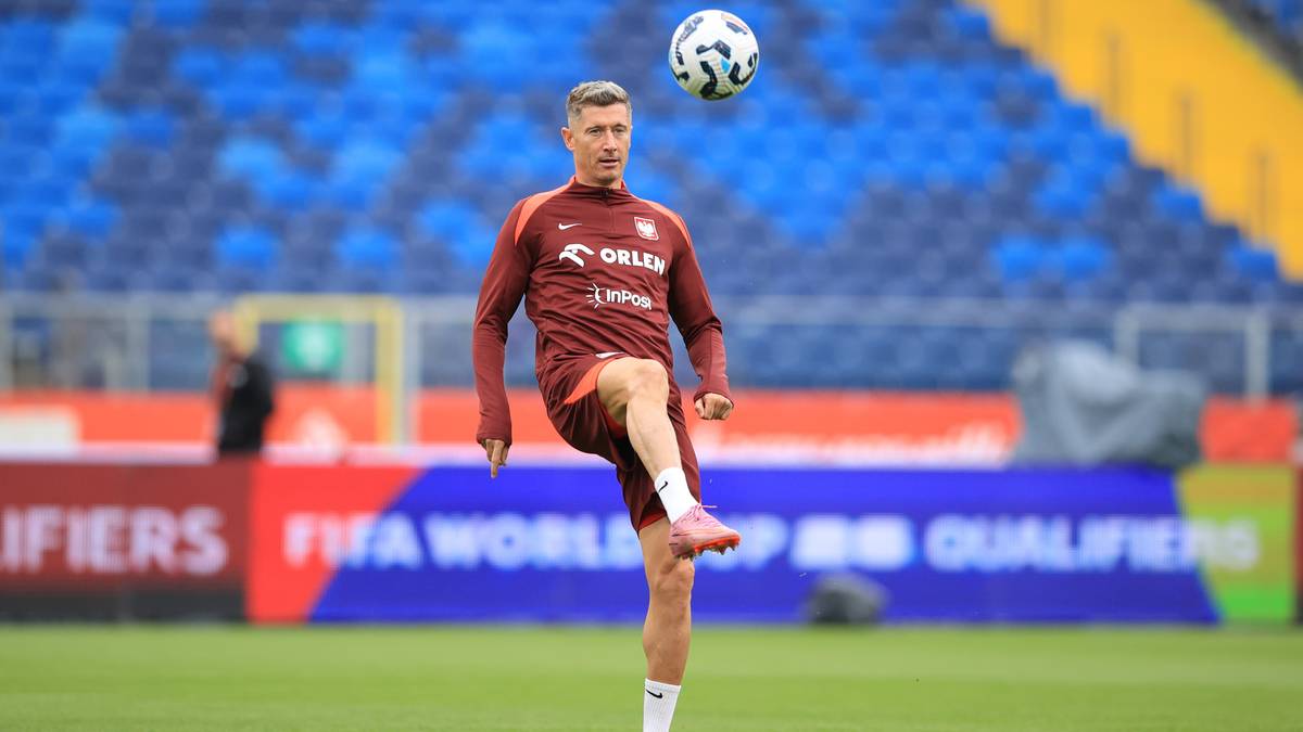 Piłkarz Robert Lewandowski w bordowej koszulce treningowej reprezentacji Polski wykonuje ćwiczenie z piłką nożną na stadionie.