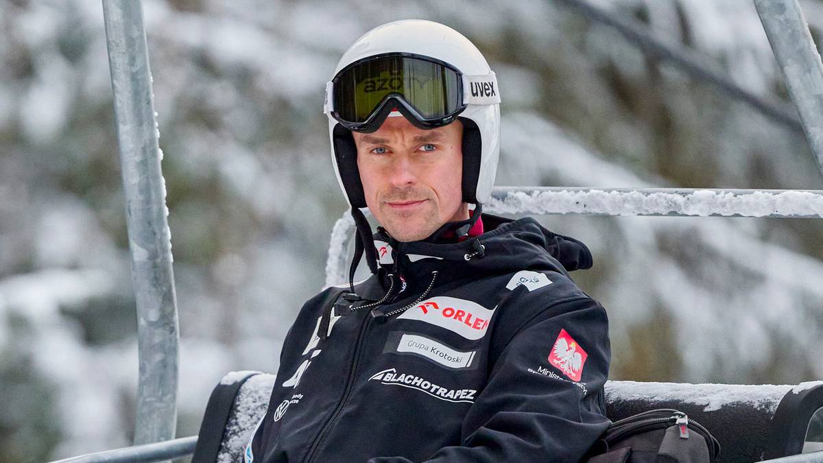 Skoczek narciarski w białym kasku i goglach na wyciągu krzesełkowym