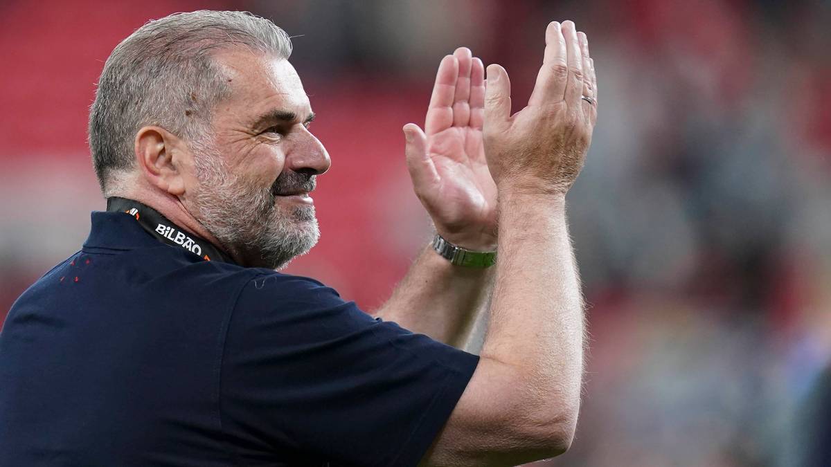 Uśmiechnięty mężczyzna w średnim wieku z siwiejącą brodą i włosami, ubrany w ciemną koszulkę polo, klaszcze w dłonie.