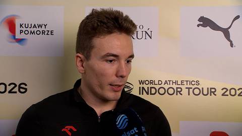 Jakub Szymański podczas wywiadu, w tle banery z logotypami i nazwami wydarzeń sportowych.