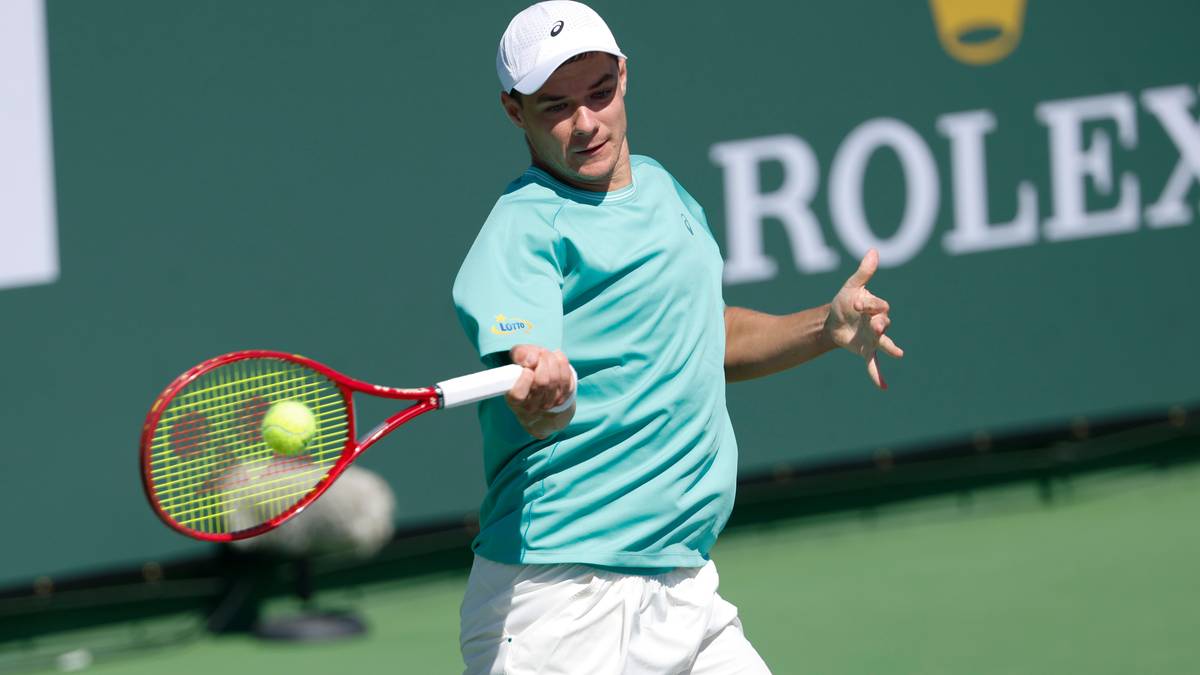 Tenisista w turkusowej koszulce i białych spodenkach uderza piłkę rakietą tenisową.