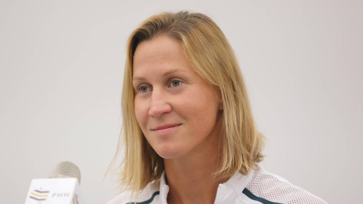 Portret uśmiechniętej kobiety z blond włosami i niebieskimi oczami, patrzącej w lewo. Na jej twarzy widać ślady makijażu. W tle neutralna jasna ściana.