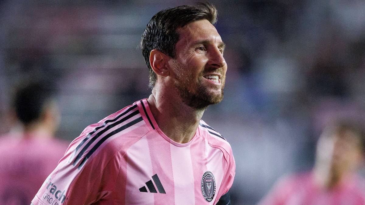 Leo Messi w różowej koszulce piłkarskiej z białymi paskami, patrzący w prawo z otwartymi ustami.