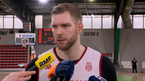 Michał Sokołowski, polski koszykarz, udziela wywiadu, ubrany w str&oacute;j sportowy, stoi w hali sportowej z mikrofonami przed twarzą.