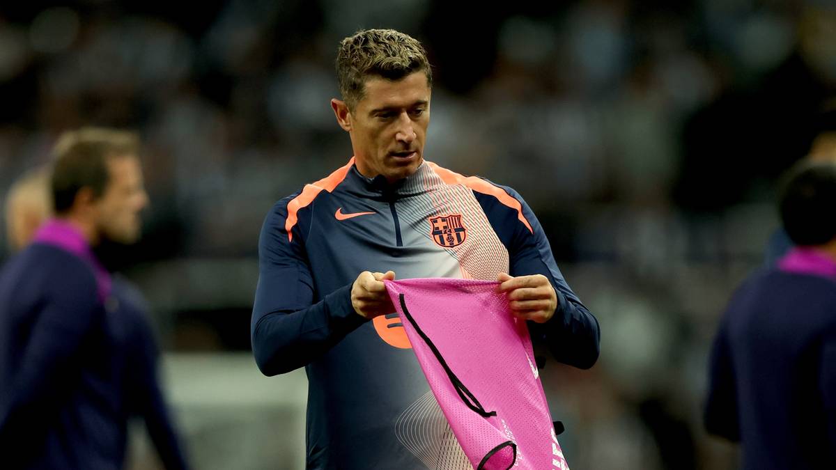 Piłkarz Robert Lewandowski w stroju Barcelony trzyma w rękach różową koszulkę.