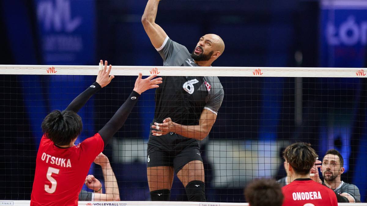 Siatkarz w szarym stroju z numerem 6 wyskakuje do ataku, próbując ominąć blok przeciwnika. Po drugiej stronie siatki, gracz w czerwonej koszulce z numerem 5 próbuje go zatrzymać.