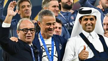 Trzej mężczyźni w garniturach i stroju sportowym świętują razem sukces, jeden z nich ma na szyi złoty medal.