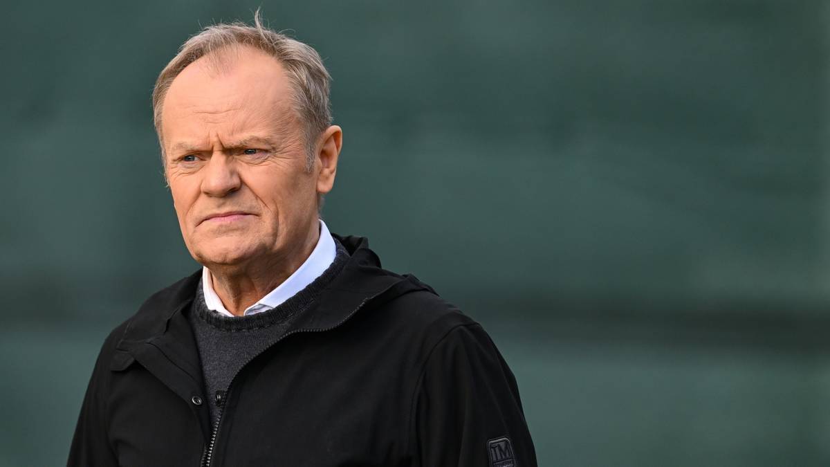 Donald Tusk, premier Polski, ubrany w czarną kurtkę i sweter, patrzy w bok z poważnym wyrazem twarzy.