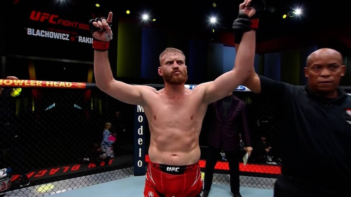 Jan Błachowicz z uniesionymi rękami w geście zwycięstwa na tle hali sportowej UFC.