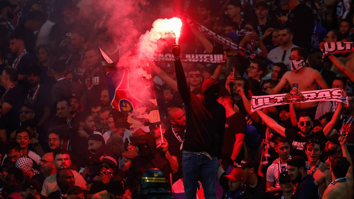 Tłum kibic&oacute;w z płonącymi racami i flagami na stadionie.