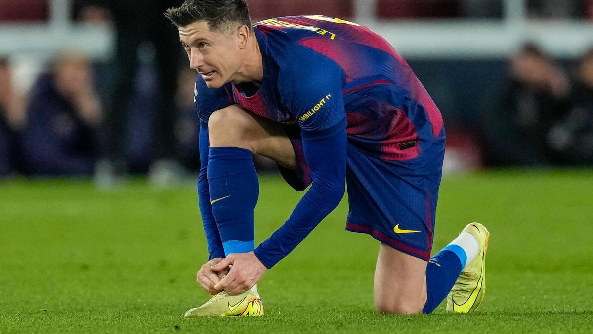 Piłkarz Robert Lewandowski w niebiesko-czerwonym stroju FC Barcelony klęczy na murawie i sznuruje but.