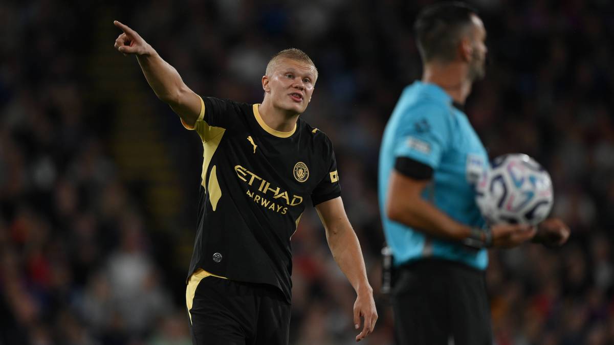 Piłkarz Erling Haaland w stroju Manchesteru City wskazuje palcem w g&oacute;rę podczas meczu.