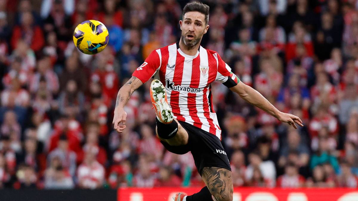 Piłkarz w czerwono-białym stroju z numerem 19 na plecach kopie piłkę w powietrzu podczas meczu.