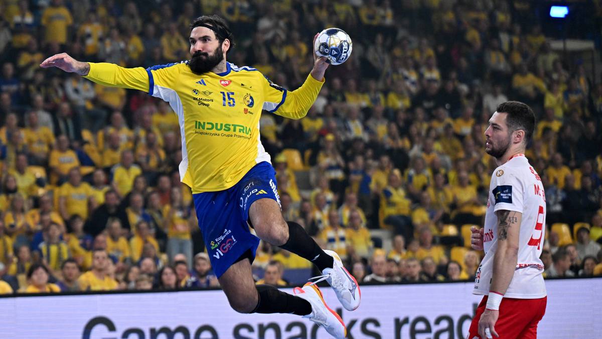 Zawodnik piłki ręcznej w skoku do rzutu w żółtej koszulce z numerem 16, obok zawodnik w białej koszulce, w tle trybuny kibiców.