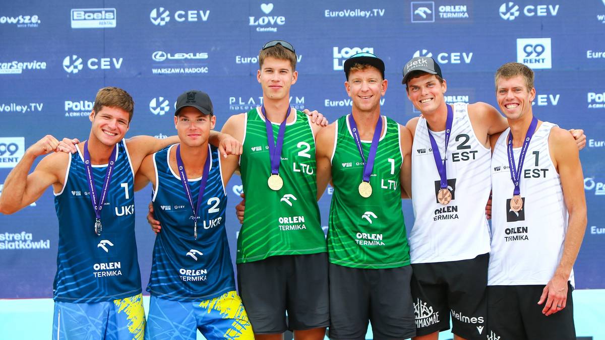 Drużyna siatkarzy plażowych w strojach sportowych z medalami na szyjach i w okularach przeciwsłonecznych.