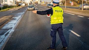 Policjant w kamizelce odblaskowej kieruje ruchem na drodze.