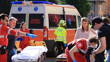 Ratownicy medyczni udzielają pomocy poszkodowanym na ulicy, w tle widoczna karetka pogotowia z napisem "MODENA SOCCORSO".