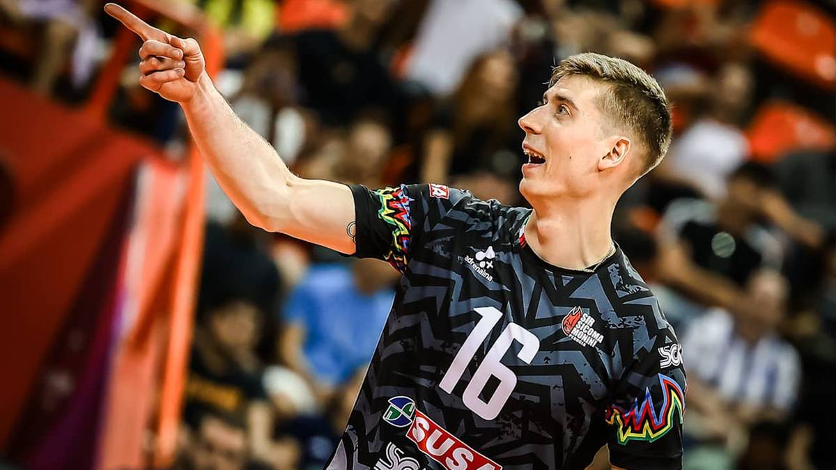 Siatkarz w czarno-szarej koszulce z numerem 16 wskazuje palcem w g&oacute;rę.