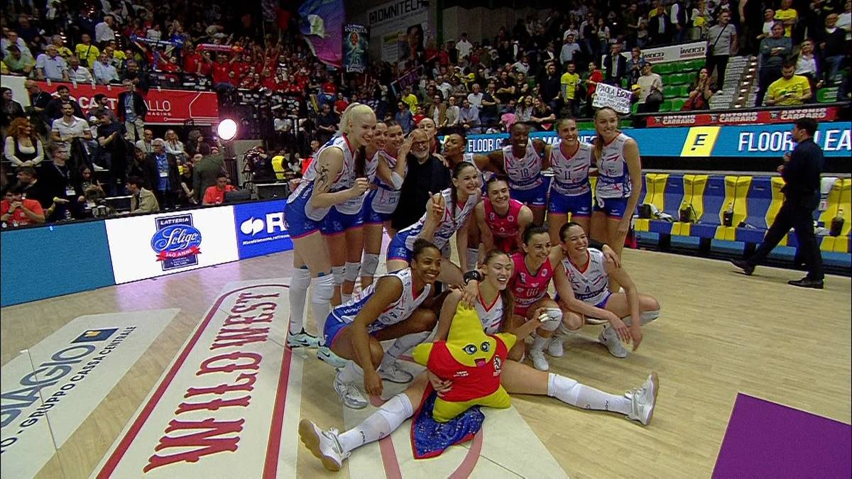 Siatkarki Imoco Volley Conegliano świętujące zwycięstwo, siedzące na parkiecie z pucharem.