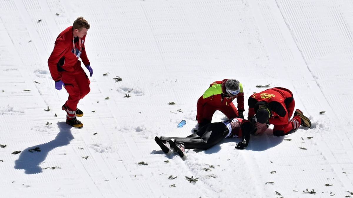 Ratownicy udzielają pomocy upadłemu skoczkowi narciarskiemu na śnieżnym zeskoku.