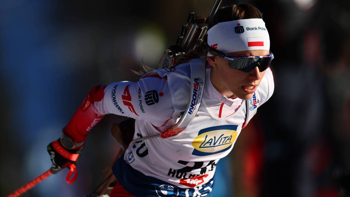 Biathlonistka podczas zawod&oacute;w, ubrana w białą czapkę z polską flagą, okulary ochronne i biało-czerwoną kamizelkę z numerem startowym.