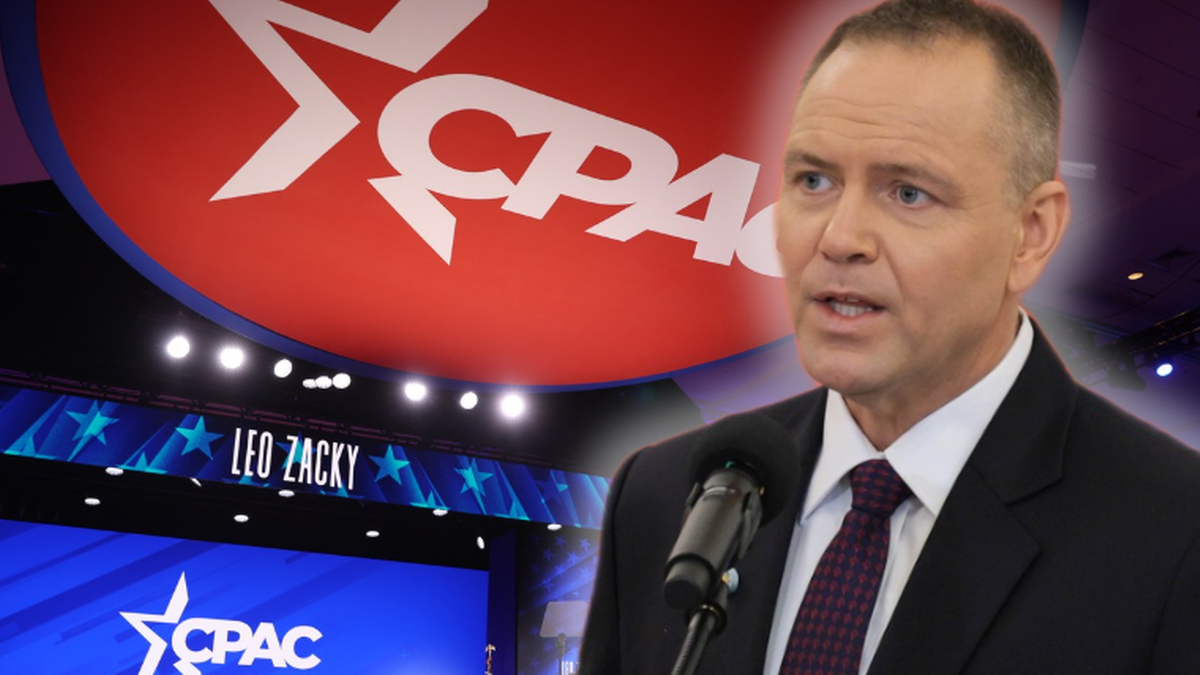 Mężczyzna w garniturze mówi do mikrofonu na tle sceny z logo CPAC.