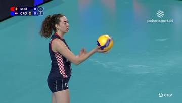 Siatkarka w stroju z numerem 12 trzyma piłkę do siatk&oacute;wki w prawej dłoni, przygotowując się do serwisu. Na ekranie widać wynik meczu Rumunia - Chorwacja.