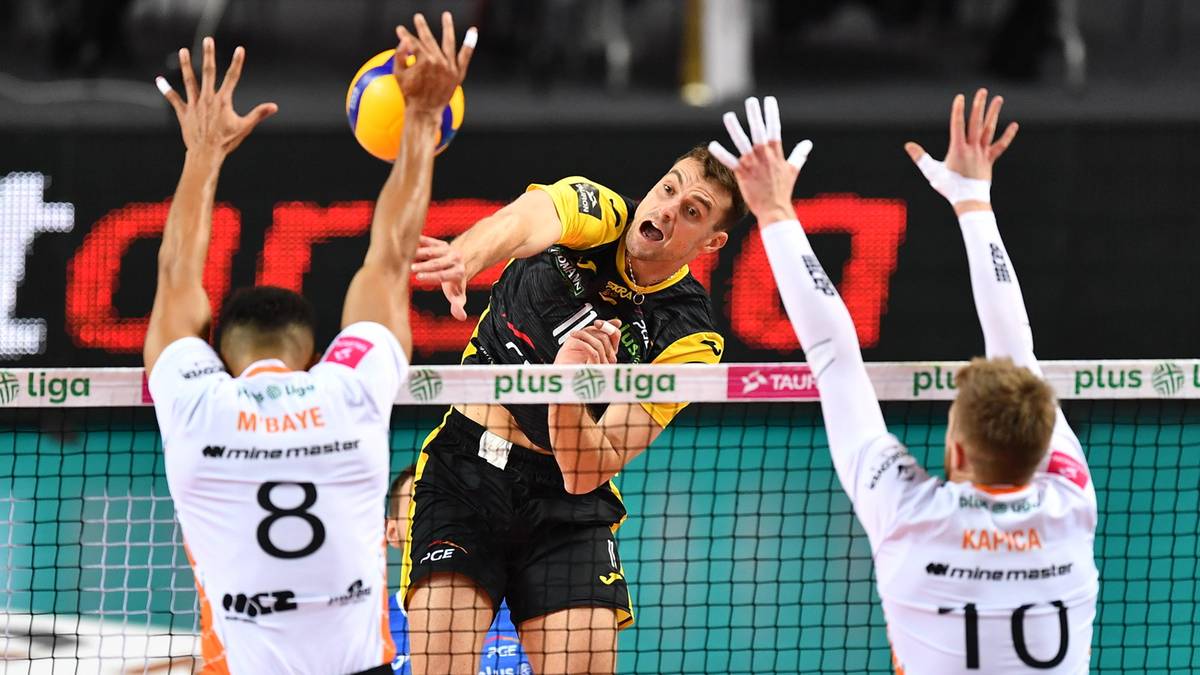 Siatkarze blokują atakującego zawodnika podczas meczu.