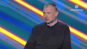 Mężczyzna w ciemnej bluzie z kołnierzykiem na tle abstrakcyjnego, kolorowego tła.