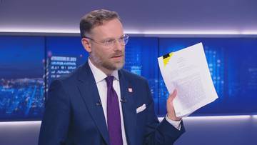 Mężczyzna w garniturze i krawacie trzyma dokument.