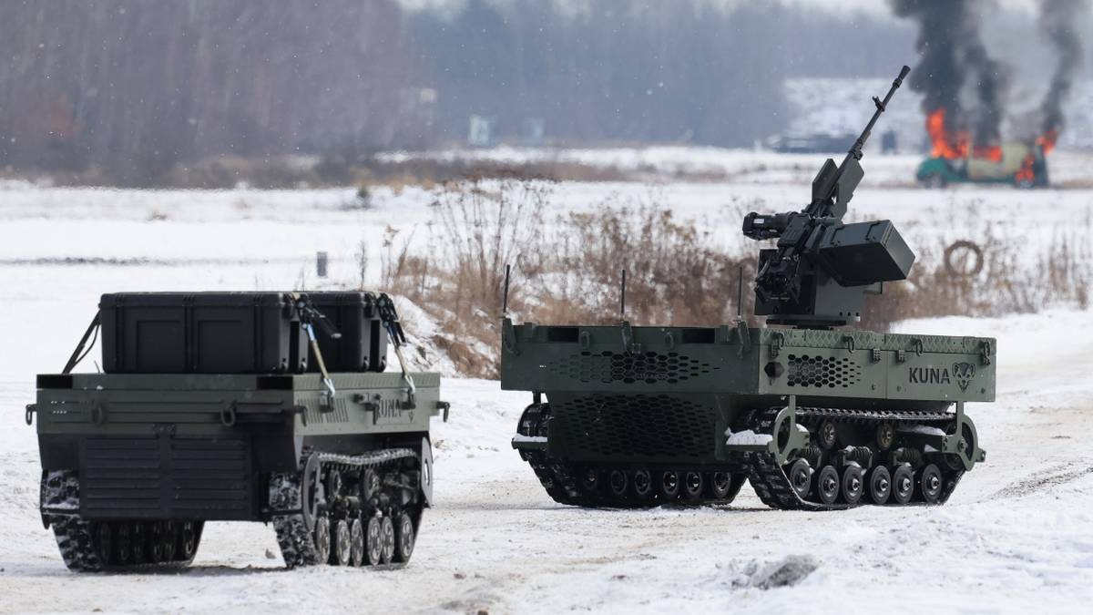 Dwa pojazdy wojskowe na zaśnieżonym polu, w tle płonący budynek z dymem.