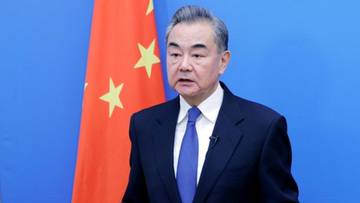 Mężczyzna w garniturze i krawacie stoi przed flagą Chin.