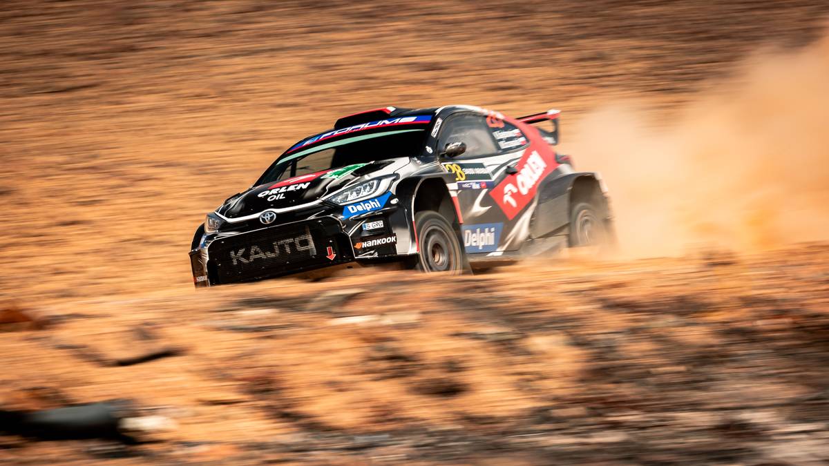 Samochód rajdowy z numerem 22 i logotypami ORLEN Rally Team i Delphi na piaskowej nawierzchni, unoszący kurz.