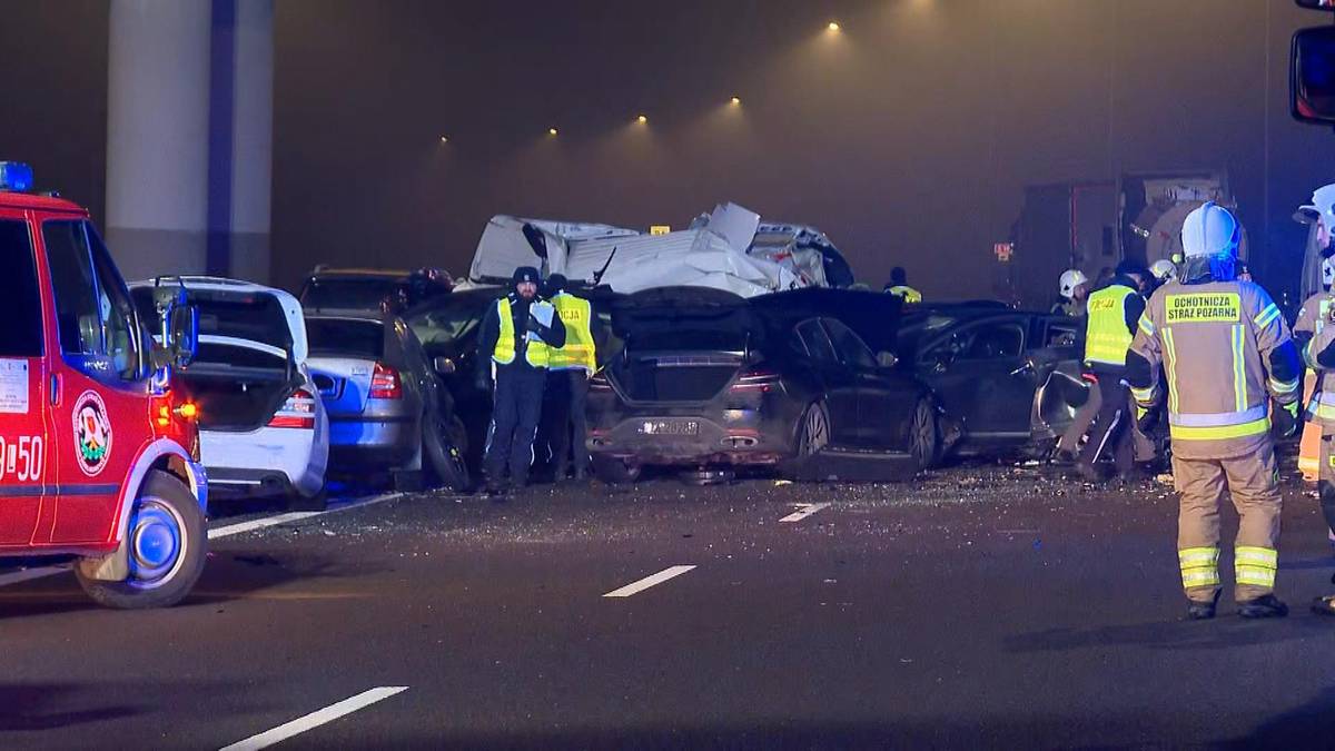 Na drodze w nocy, w gęstej mgle, doszło do karambolu z udziałem wielu samochodów. Widać służby ratunkowe i zniszczone pojazdy.